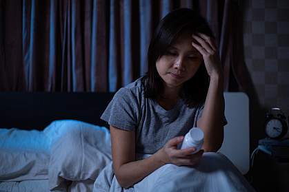 Woman sitting up in bed and looking at a pill bottle. Woman sitting up in bed and looking at a pill bottle.