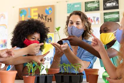 Teacher and students in a classroom wearing masks and looking at seedlings Teacher and students in a classroom wearing masks and looking at seedlings