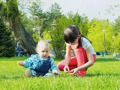 Infant boy and older sister playing in the grass Infant boy and older sister playing in the grass