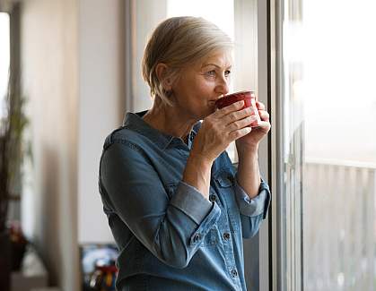 Senior woman looking out a window sipping a cup of tea Senior woman looking out a window sipping a cup of tea
