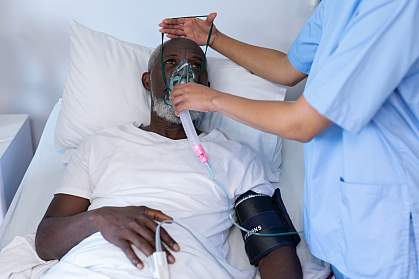 Medical worker putting oxygen mask on a senior Black man in a hospital bed Medical worker putting oxygen mask on a senior Black man in a hospital bed
