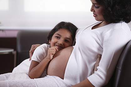 Young girl with her ear against a woman’s pregnant belly Young girl with her ear against a woman’s pregnant belly