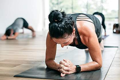 Sweating woman practicing hot yoga holding plank pose.