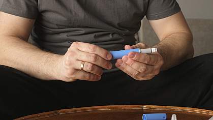 Man sitting on couch and preparing a GLP-1RA injection. Man sitting on couch and preparing a GLP-1RA injection.
