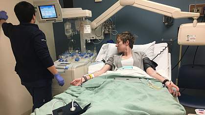 A medical technician watches the monitor of a woman with IVs in a hospital bed. A medical technician watches the monitor of a woman with IVs in a hospital bed.