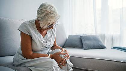 Senior woman on a couch holding her knee in pain. Senior woman on a couch holding her knee in pain.