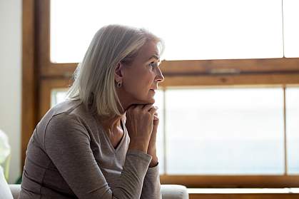 Side view of thoughtful middle-aged mature woman sitting on a couch at home in front of a window. Side view of thoughtful middle-aged mature woman sitting on a couch at home in front of a window.