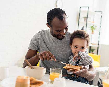 Father with young son on his lap spreading peanut butter on toast. Father with young son on his lap spreading peanut butter on toast.