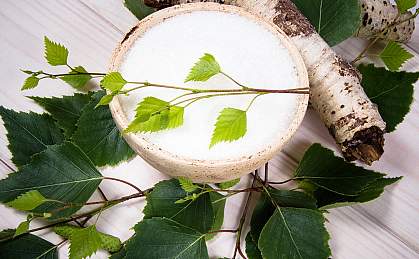 Xylitol crystals in a birch bowl beside a birch branch with leaves Xylitol crystals in a birch bowl beside a birch branch with leaves.