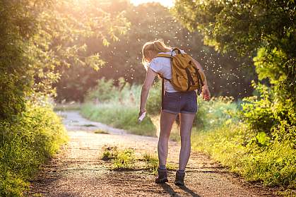 Woman on a hike in the forest applying insect repellent as mosquitoes swarm around her. Woman on a hike in the forest applying insect repellent as mosquitoes swarm around her.