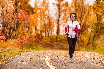Middle-age Asian woman running on a park path through autumn foliage. Middle-age Asian woman running on a park path through autumn foliage.