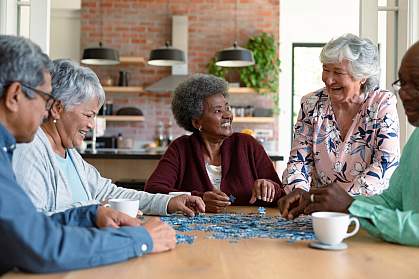 Diverse group of older people socializing while doing a puzzle. Diverse group of older people socializing while doing a puzzle.