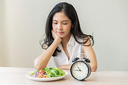 Young woman gazing at a salad beside an alarm clock showing 10:45. Young woman gazing at a salad beside an alarm clock showing 10:45.