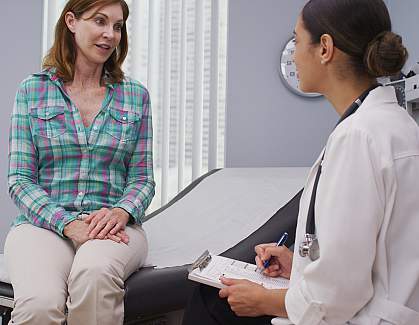 Middle-aged woman sitting on an examination table talking to a younger woman doctor.
