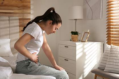 Young woman sitting on bed and clutching her stomach in pain. Young woman sitting on bed and clutching her stomach in pain.