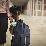 Photo from the back of a child holding tightly to and leaning on a parent's arm.