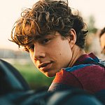 Close-up of a teenage boy sitting outside with friends, looking at the camera.