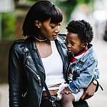 Black woman holding a toddler and walking down a city street.